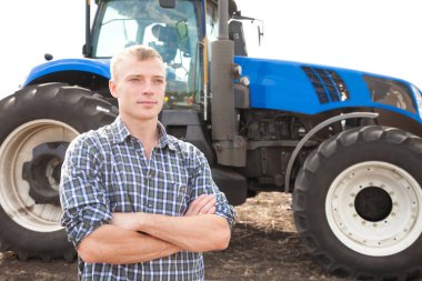 Genç çekici bir adam traktörün yanında. Traktör sürücüsü. Tarım ve saha çalışmaları kavramı.