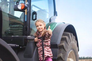 Tarladaki modern traktörün yanında tatlı bir kız. Saha çalışması konsepti, tarım makineleri.