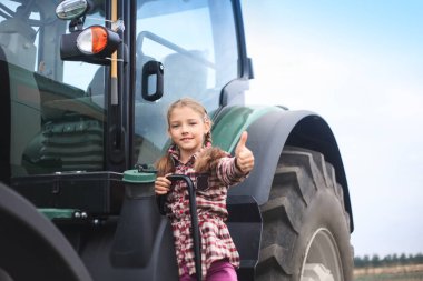 Tarladaki modern traktörün yanında tatlı bir kız. Saha çalışması konsepti, tarım makineleri.