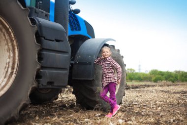 Tarladaki modern traktörün yanında tatlı bir kız. Saha çalışması konsepti, tarım makineleri.