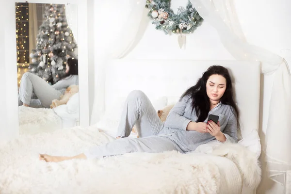 Jonge mooie vrouw in bed met een mobiele telefoon in haar handen. — Stockfoto