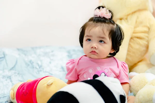 1 yaşında pembe elbiseli bir kız çocuğu Bangkok Tayland 'da yatakta oyuncak ayıyla oynuyor..