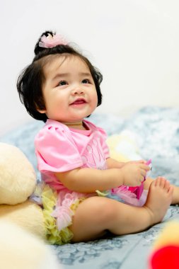 1 yaşında pembe elbiseli bir kız çocuğu Bangkok Tayland 'da yatakta oyuncak ayıyla oynuyor..
