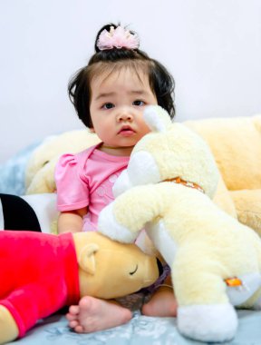 Güzel bir kız bebek oyun konsepti, pembe elbiseli bir bebek oyuncak ayı ve oyuncakla oynuyor çok mutlu komik ve Bangkok Tayland, Asya 'da yatakta gülümsüyor.