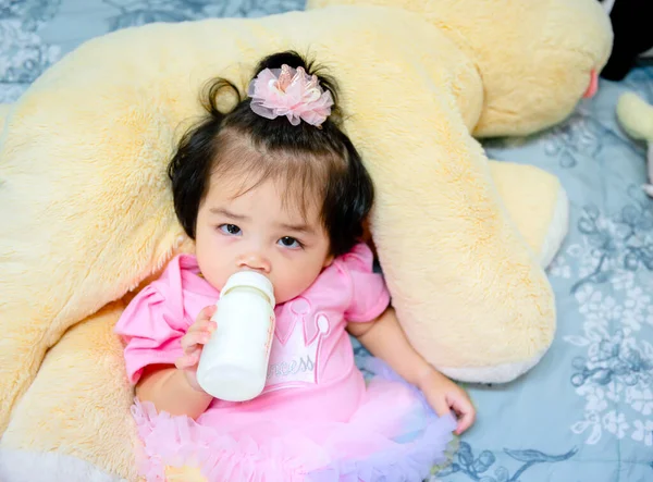 Güzel bir kız bebek oyun konsepti, pembe elbiseli bir bebek oyuncak ayı ve oyuncakla oynuyor çok mutlu komik ve Bangkok Tayland, Asya 'da yatakta gülümsüyor.
