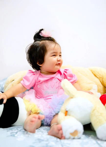 Güzel bir kız bebek oyun konsepti, pembe elbiseli bir bebek oyuncak ayı ve oyuncakla oynuyor çok mutlu komik ve Bangkok Tayland, Asya 'da yatakta gülümsüyor.