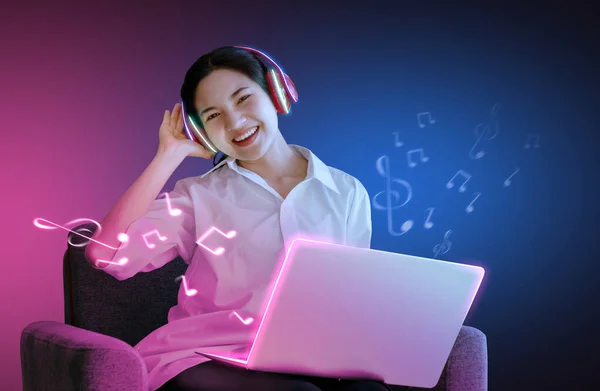 The girl is listening to the song sing with laptop on sofa, smiling face In the studio Which has various colors of light And the pink background
