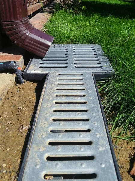 drainage systems. idea - building a house, storm taps. metal construction from the roof - sewer and grate on the ground for draining water closeup. sunny day, green grass