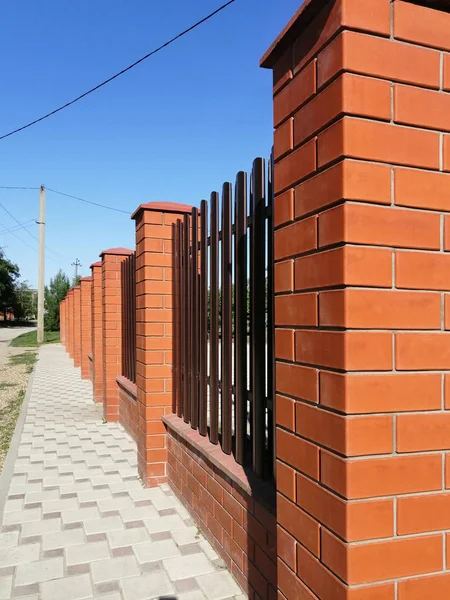 fence of red brick and metal vertical stripes - shtaketin. perspective view against the blue sky. idea - building a private house