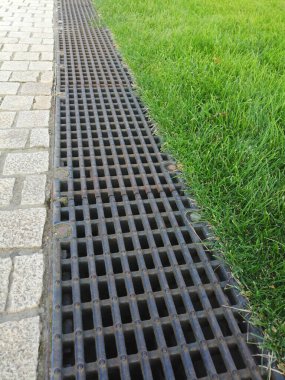 Kanalizasyon sistemleri. Su drenajı için metal yapılar - kanalizasyon ve yerde ızgara. Ev yapımı, fırtına vinçleri. Yeşil çimenler ve kaldırım taşları. Grünn 'de peyzaj ve çardak