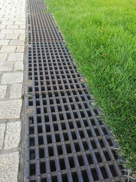 Kanalizasyon sistemleri. Su drenajı için metal yapılar - kanalizasyon ve yerde ızgara. Ev yapımı, fırtına vinçleri. Yeşil çimenler ve kaldırım taşları. Grünn 'de peyzaj ve çardak