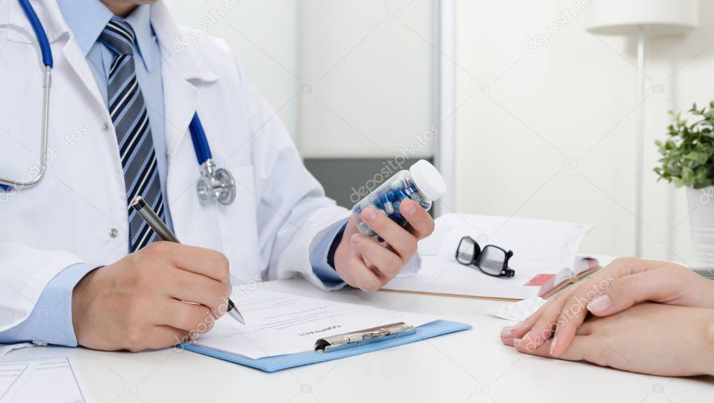 Doctor and patient at office. Doctor prescribes the recipe. Holding bottle of pills.