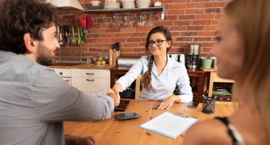 Adam elini sıkarken emlakçı. Genç bir çift için ev sahipliği sunuyoruz.