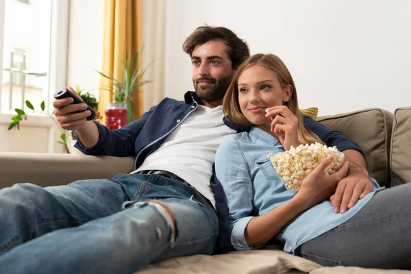 Couple watching TV, eating popcorn on a sofa at home