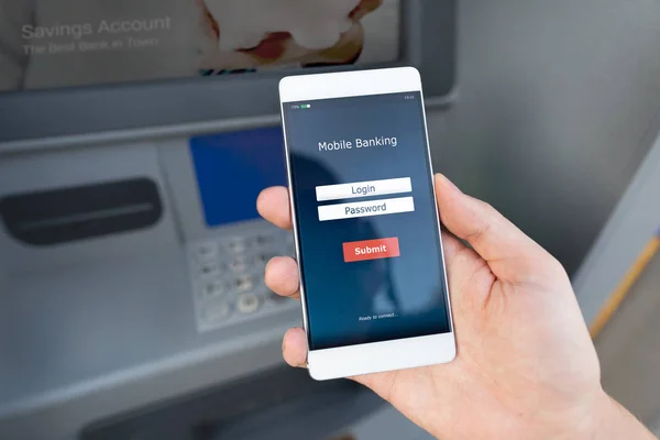 Withdraw money from an ATM without using a credit card. Person holding a phone with a login screen for mobile banking.