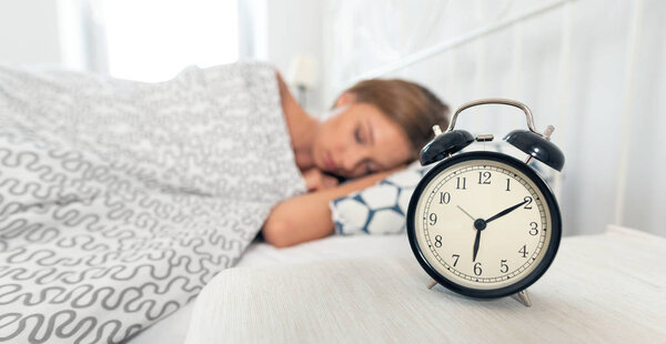 Young woman is sleeping in her bed. Alarm clock in the foreground