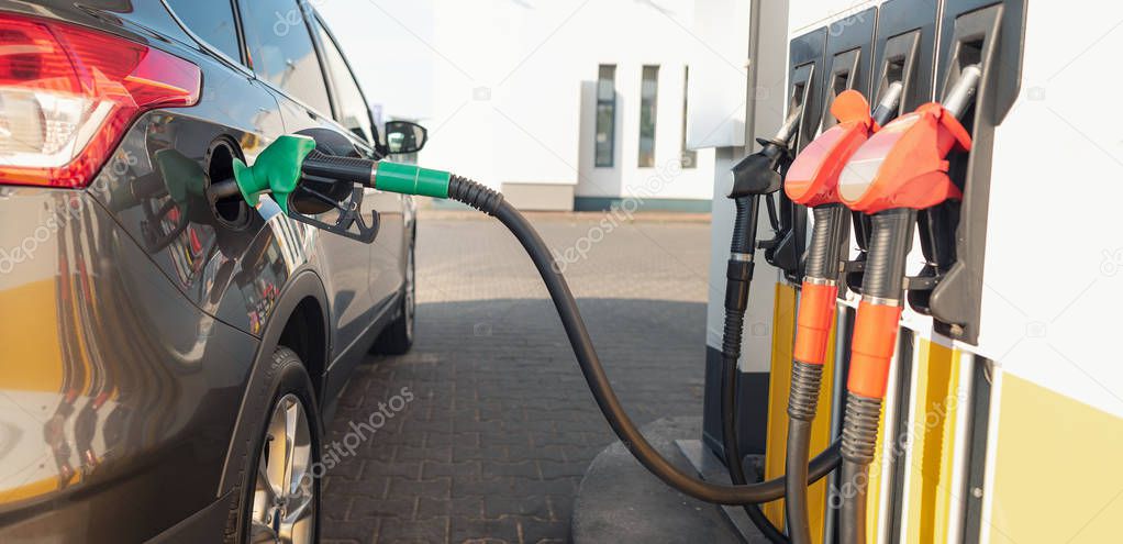 Gas pump nozzle in the fuel tank of a gray car. Refueling the vehicle at a gas station