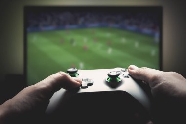 Adam konsolda oynuyor. Gamepad tutarak ve futbol oyunu oynarken adam