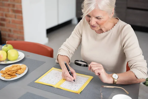 Senior vrouw geniet van het oplossen van een kruiswoordpuzzel — Stockfoto