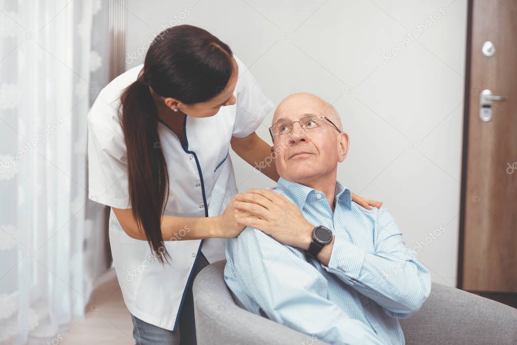 Smiling nurse and old senior man patient at home