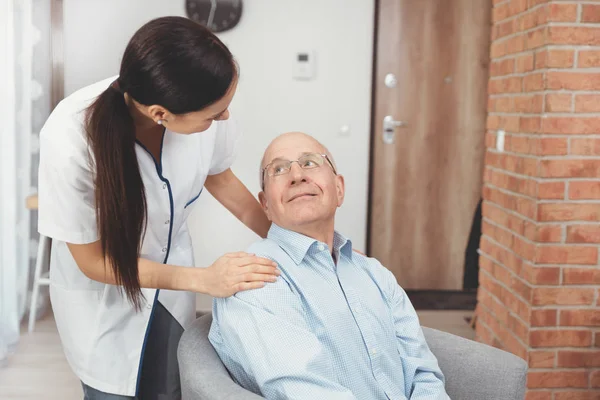 Glimlachende verpleegkundige en oude Senior man patiënt thuis — Stockfoto