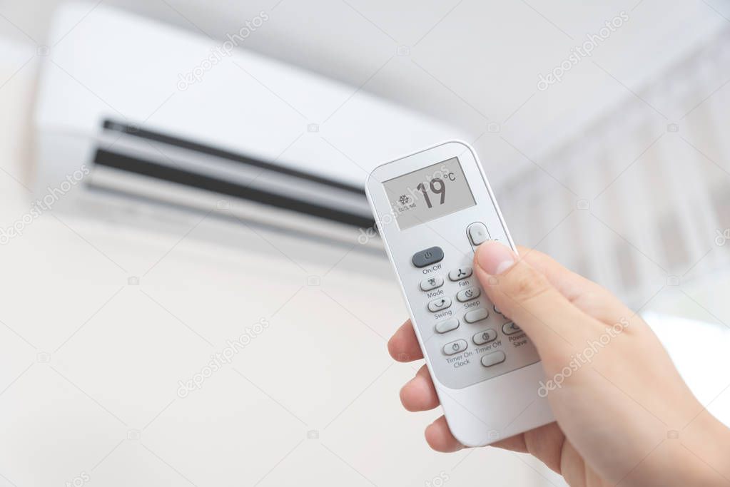 Hand with remote directed on air conditioner.