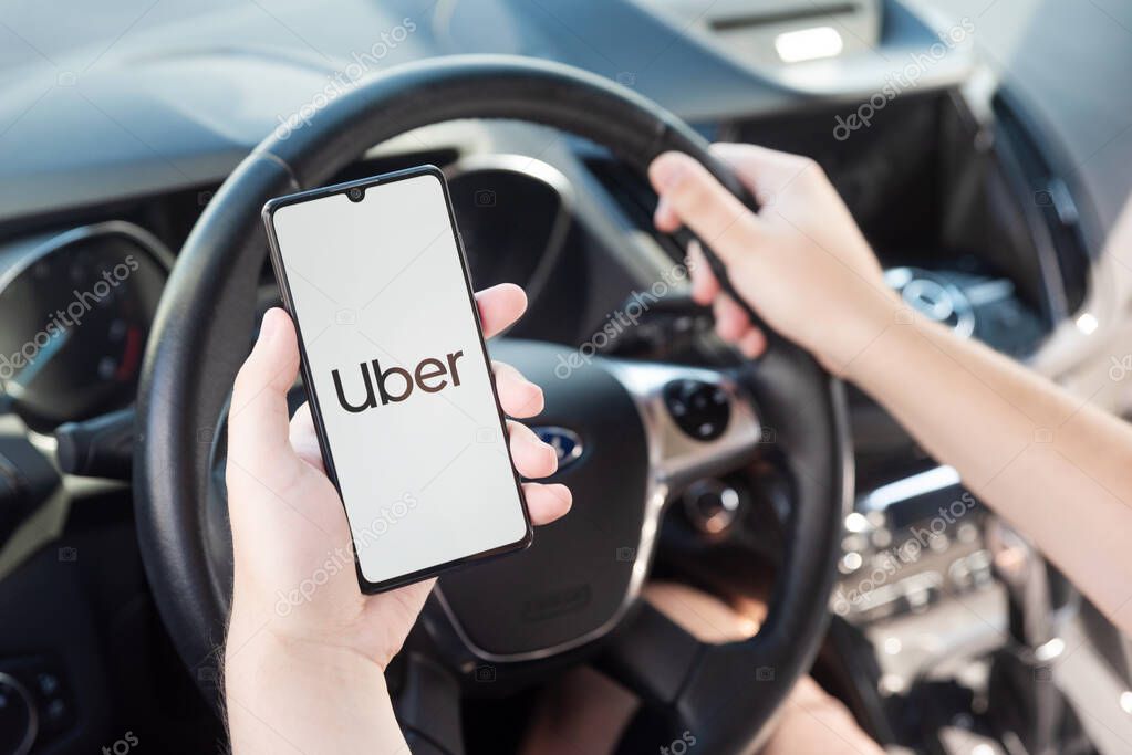 Wroclaw, Poland - AUG 25, 2020: Uber driver holding smartphone in car. Uber is sharing-economy service for ubran transport.