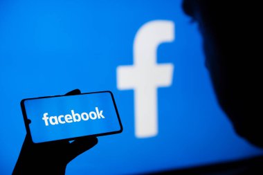 Wroclaw, Polonya - SEP 16, 2020: Facebook mobil uygulamalı akıllı telefonu olan adam, Facebook logosu arka planda. Facebook en popüler sosyal medya hizmetidir.