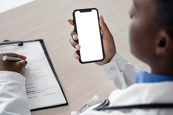 African doctor holding using phone mock up white screen, over shoulder close up.