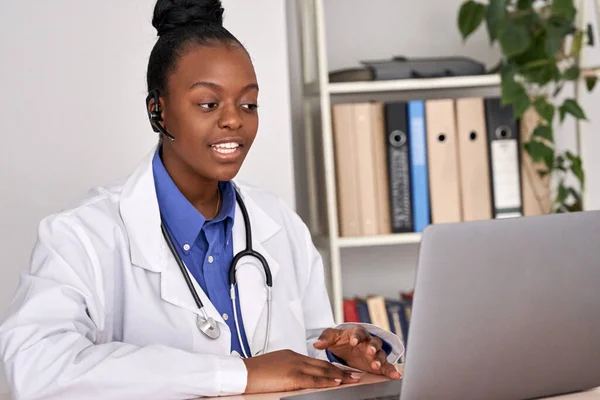 African female doctor talk to patient by online webcam video call on laptop.