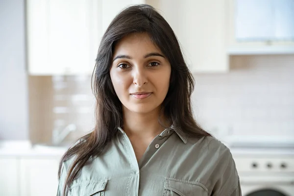 Confident young indian woman looking at camera at home in kitchen, headshot.