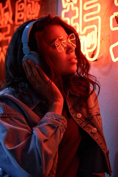 African American lady wearing headphones listening music in neon light.