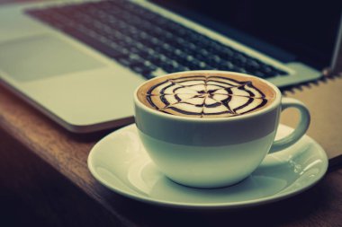 Masanın üstünde laptop ile birlikte yerleştirerek sıcak latte kahve Kupası kapatın