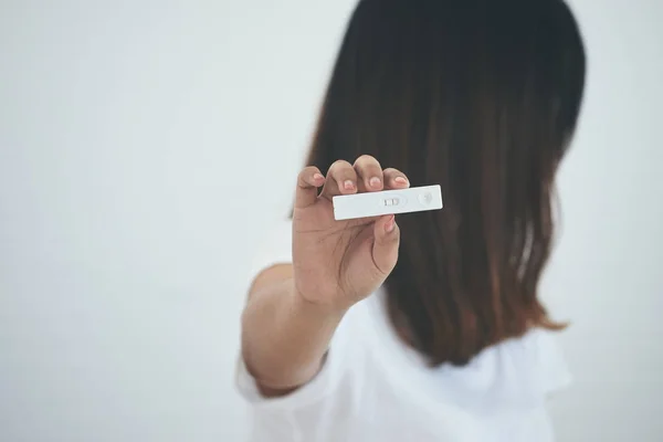 Teenager holding pregnancy test cassette with positive result on white background; Unintended pregnancy concept