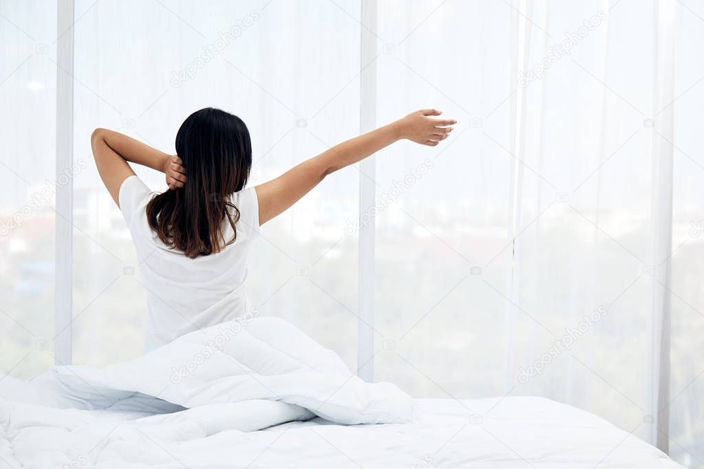 Asian Teenager stretching on bed while wake up early in Morning