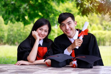 Parkta mezun töreni için mezuniyet kıyafeti giyen arkadaşları ile Mezun güzel genç Asyalı öğrenci Kavramı