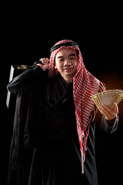 黒い背景に隔離されたドル紙幣を見ながら スーツケースを持ち 微笑むアラブのビジネスマン — ストック写真