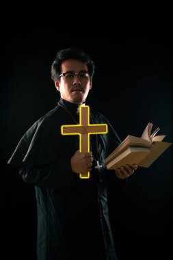 Koyu ton, jant ışığı - Rahip siyah arka planda hayalet kovmak için İncil 'i tutarken haç yakıyor