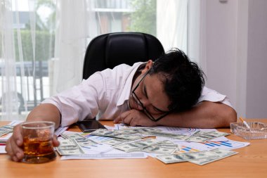 Yorgun işadamı, etrafa saçılmış dolarlarla çevrili mali belgelerde uyuyor. Elinde bir bardak viski, stresi ve tükenmişliği simgeliyor.