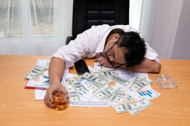 Aşırı çalışan iş adamı, elinde bir bardak viski, stres, açgözlülük ve finansal baskıyı simgeleyen dağınık paralarla mali raporlarda uyuyor.