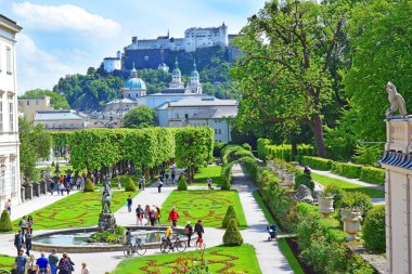 Salzburg, Avusturya - 23 Mayıs 2018 : Salzburg'daki Mirabell parkında çiçek yatakları arasında yürüyen insanlar, arka planda eski tarihi Kale Hohensalzburg