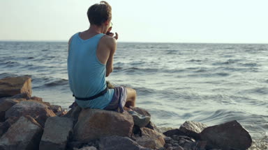 Erkek gömlek ve mızıka sahilde oynarken güneş gözlüğü. Arkadan görüntülemek.