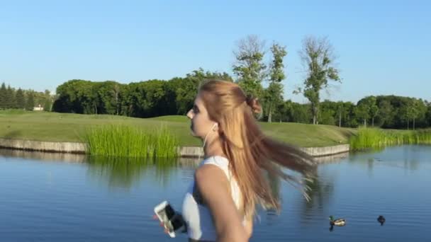 Femme Dans Les Écouteurs Tenant Smartphone Courir Près Lac — Video