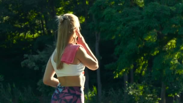 ヘッドフォンでの女性のフィットネスは 訓練の後音楽と飲料水に耳を傾ける — ストック動画