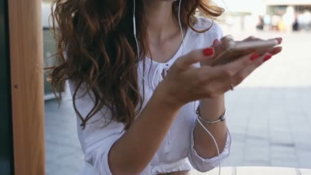 美丽的卷发妇女在耳机持有智能手机和短信 — 图库视频影像