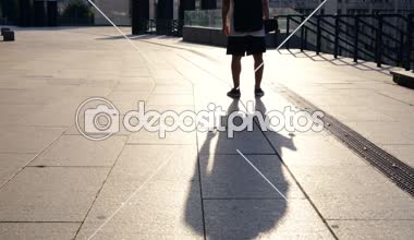 Sırt çantası ve kaykay street yürüyüş olan genç adam. Arkadan görüntüleyin. Sürekli çekim.