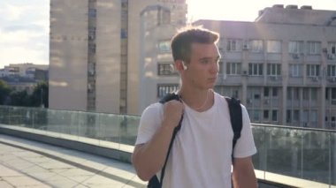Genç adam street yürüyüş ve kulaklık müzik dinlemek sırt çantası ile. Sabit cam vurdu.