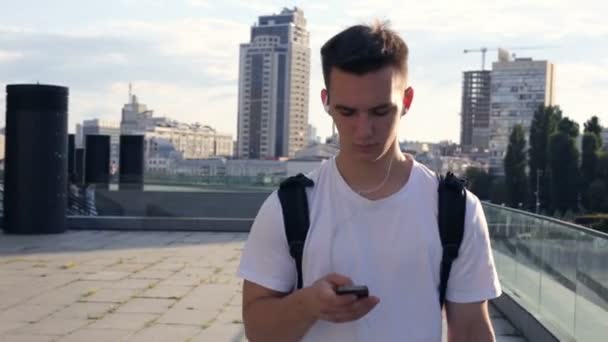 Joven Con Auriculares Sosteniendo Teléfono Inteligente Mirándolo Enviando Mensajes Texto — Vídeos de Stock