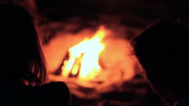 Kamp ateşi yanında oturan bir çift gördüm. Adam holding smartphone. Gece vakti. Arkadan görüntülemek.