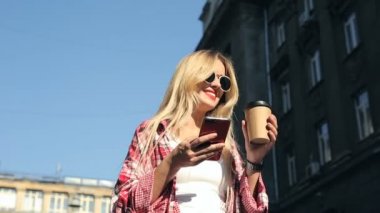 Hareket eden telefon, mesaj ve drinkig kahve tutan mutlu, gülümseyen kadın. Steadycam atış.